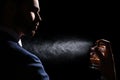 Man spraying luxury perfume on black background, closeup