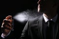 Man spraying luxury perfume on black background, closeup