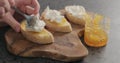 Man spreading riccotta over orange marmalade on ciabatta slices on wood board