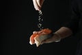 Man sprinkle salt on salmon meat on dark background