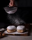 Man sprinkles powdered sugar on two donuts, on a wooden table and black background Royalty Free Stock Photo