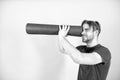 Man spy in yoga mat as telescope. Fashion athlete in blue tshirt and shorts. Sportsman with stylish bristle and hair