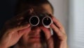 The man is spying on people, using binoculars
