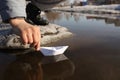 A man squatting launches a paper boat in a puddle in early spring