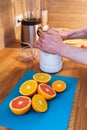 Man squeezes juice on a juicer from chopped red and orange oranges in the kitchen