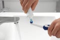 Man squeezing toothpaste from tube onto electric toothbrush above sink, closeup Royalty Free Stock Photo