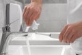 Man squeezing toothpaste from tube onto electric toothbrush in bathroom, closeup Royalty Free Stock Photo