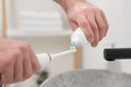 Man squeezing toothpaste from tube onto electric toothbrush indoors, closeup Royalty Free Stock Photo