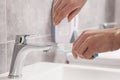 Man squeezing toothpaste from tube onto toothbrush above sink in bathroom, closeup Royalty Free Stock Photo