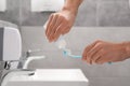 Man squeezing toothpaste from tube onto toothbrush in bathroom, closeup Royalty Free Stock Photo