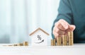 Man is stacking coins on a table, arranging them from smallest to largest, with a wooden house model beside him. Emphasizes the