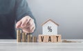 Man is stacking coins on a table, arranging them from smallest to largest, with a wooden house model beside him. Emphasizes the