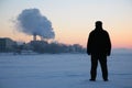 Man stand on frozen river near smoking pipes