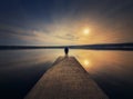 Man standing alone on the pier facing the sunset reflected in the calm lake water. Scenic view with a lonely person on the dock Royalty Free Stock Photo