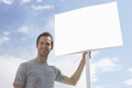 Man with standing by blank sign against cloudy sky Royalty Free Stock Photo