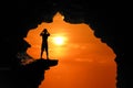 The man standing in a cave on a high cliff at red sky sunset Royalty Free Stock Photo