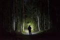 Man standing in dark forest at night with flashlight and hoodie on head