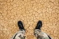 Man standing on a dry cracked earth. Feet in sneakers and in military pants standing on the cracked soil Royalty Free Stock Photo