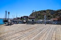 A man standing on the edge of a long brown wooden pier fishing surrounded by docked boats in the harbor and lush green trees Royalty Free Stock Photo