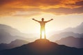 Man standing on edge of mountain feeling victorious with arms up in the air.