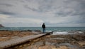 Man standing at the edge of a wooden pier in the stormy sea at sunset. Feeling free. Waves splashing on rocky coast Royalty Free Stock Photo