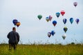 Man standing in the field and looking at colorful hot air balloo