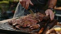 A man is standing by a grill, cutting pieces of meat with a knife