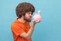 Man standing holding looking at piggybank with dollar banknotes with frowning face.