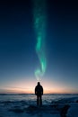 A man standing on the ice and looking at sunset and aurora