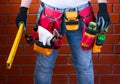 Man with standing level in his hand against the background of a red brick wall with a full tool bag. DIY Royalty Free Stock Photo