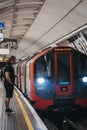 Man standing on a London Underground station platform using his phone, train passing by, motion blur Royalty Free Stock Photo