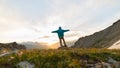 Man standing on mountain top outstretching arms, sunrise light colorful sky scenis landscape, conquering success leader concept.