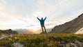 Man standing on mountain top raising arms, sunrise light colorful sky scenis landscape, conquering success leader concept.