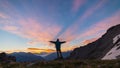 Man standing on mountain top raising arms, sunrise light colorful sky scenis landscape, conquering success leader concept.