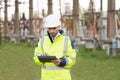 Man standing near high voltage substation and typing on device. Male engineer in uniform and helmet standing outdoor and