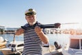 Man standing near the sea dressed in a sailor`s shirt and hat holding a harpoon