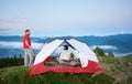 Man standing near the tent in which sits woman against beautiful scenery of mighty mountains