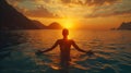A man standing in the ocean with arms spread wide, facing a sunset between mountainous islands Royalty Free Stock Photo