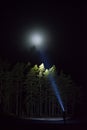 Man standing outdoor at night shining with flashlight up the sky and at trees in forest