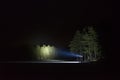 Man standing outdoor at night shining with flashlight up the sky and at trees in forest Royalty Free Stock Photo