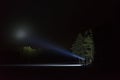 Man standing outdoor at night shining with flashlight up the sky and at trees in forest Royalty Free Stock Photo