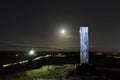 Man standing outdoors at night shining with flashlight on a metal monolith Royalty Free Stock Photo