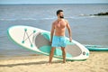 Man standing with paddle board on sandy beach near ocean , sup water sport. Royalty Free Stock Photo