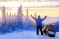 Man standing on snowy mountain near snowmobile enjoying view winter forest at sunset.