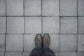 Man standing on the square shaped concrete pavement slabs, top view of dirty boots