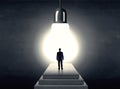 Man standing on a step in front of a huge light bulb Royalty Free Stock Photo