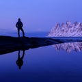 Man standing at Tungeneset, his mirror reflection in the water, mountains in the background, Senja, Troms, Norway Royalty Free Stock Photo