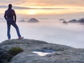 Man stands alone on the peak of rock. Hiker watching to autumn Sun at horizon