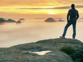 Man stands alone on the peak of rock. Hiker watching to autumn Sun at horizon