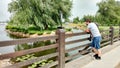 A man stands on the bridge and looks at the view: a pond, water lilies, an island with a willow, a neatly trimmed lawn Royalty Free Stock Photo